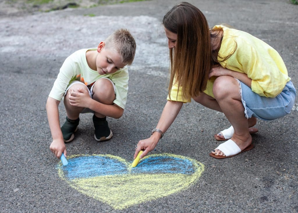 Maryana et son fils Mark, âgé de 8 ans, dessinent sur le bitume avec des craies de couleur. A cause de la guerre en Ukraine, Maryana et son fils se sont réfugiés en Allemagne après avoir échappé aux tirs d'obus dans leur pays d'origine. © UNICEF/UN0665102/Latayko