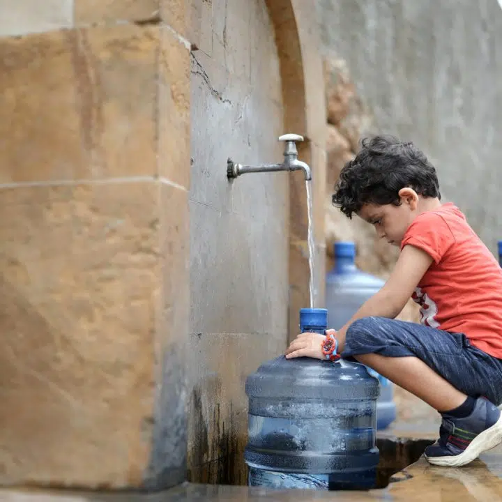 Georgio, 4 ans, aide ses parents à remplir leurs petits récipients d'eau car ils n'ont pas d'eau à la maison. © UNICEF/UN0671359/Choufany