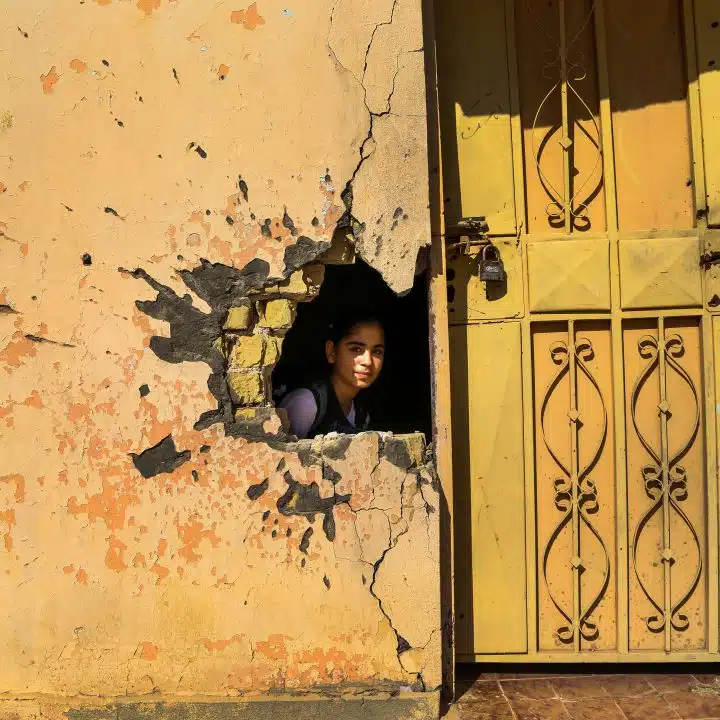 Le 1er novembre 2016, une jeune fille regarde à travers un trou dans le mur causé par les dégâts du conflit dans une école de Ramadi, dans le gouvernorat d'Anbar, en Irak. L'UNICEF travaille actuellement à la réhabilitation de 100 écoles dans l'Anbar. 3,5 millions d'enfants irakiens en âge d'être scolarisés n'ont pas accès à l'éducation, ce qui signifie qu'ils courent un risque accru de mariage précoce, de travail des enfants et d'enrôlement dans des groupes armés. Une école sur cinq n'est pas utilisée en raison du conflit. © UNICEF/UN038011/Khuzaie