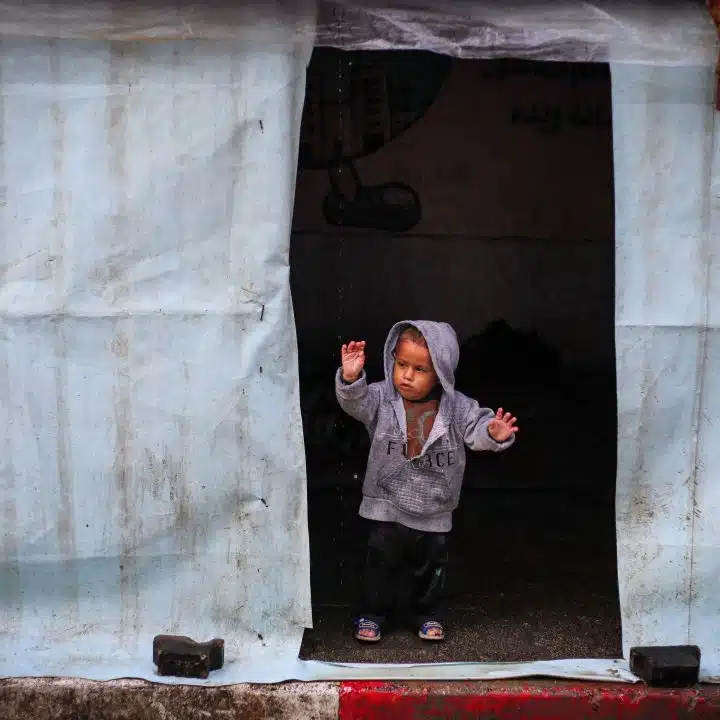 A Rafah, dans la bande de Gaza, un enfant se tient debout devant la tente qui sert de refuge à sa famille © UNICEF/UNI521732/El Baba