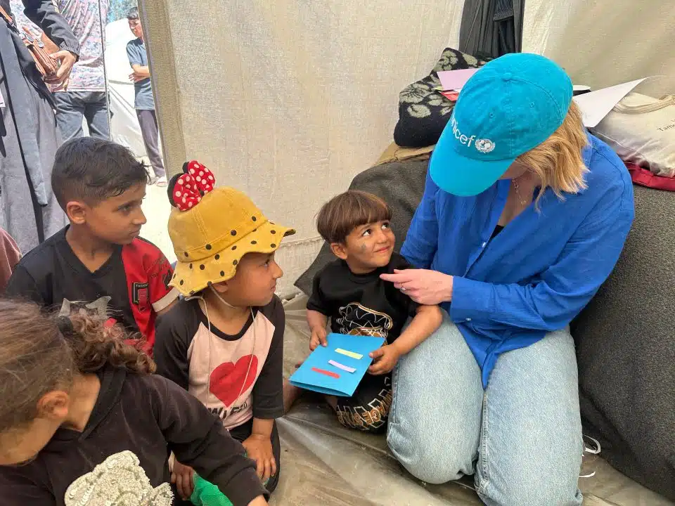 Le 3 avril 2024, à Rafah, dans le sud de la bande de Gaza, Tess Ingram, porte-parole de l'UNICEF, interagit avec des enfants participant à des activités psychosociales dans le camp de Tel al Soltan Stadium. © UNICEF/UNI551189/Eliean