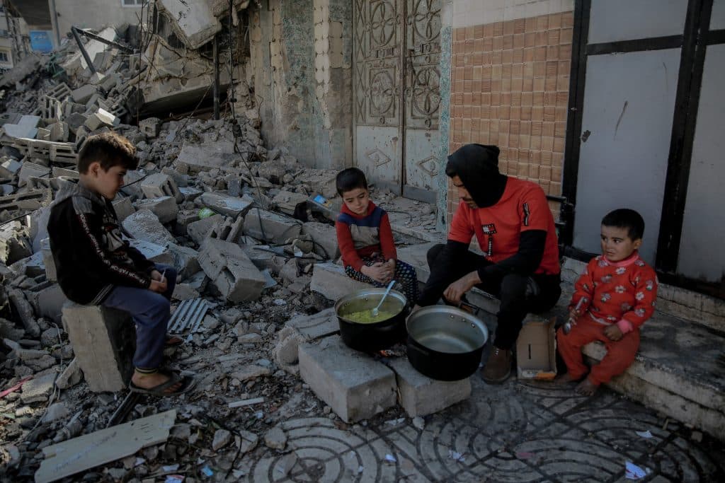 Khaled, 35 ans, entouré de ses enfants, cuisine devant sa maison détruite dans le quartier d'al-Rimal, à l'ouest de la ville de Gaza. © UNICEF/UNI501984/Al-Qattaa