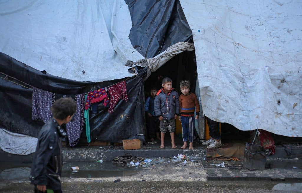 Deux enfants se tiennent pieds nus devant une tente qui leur sert de refuge dans la ville de Rafah, au sud de la bande de Gaza. © UNICEF/UNI521798/El Baba