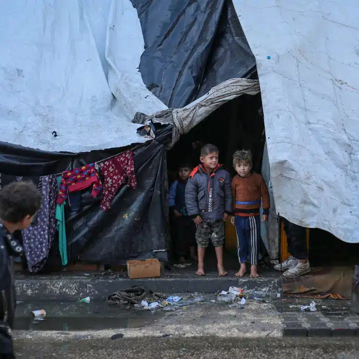 Deux enfants se tiennent pieds nus devant une tente qui leur sert de refuge dans la ville de Rafah, au sud de la bande de Gaza. © UNICEF/UNI521798/El Baba