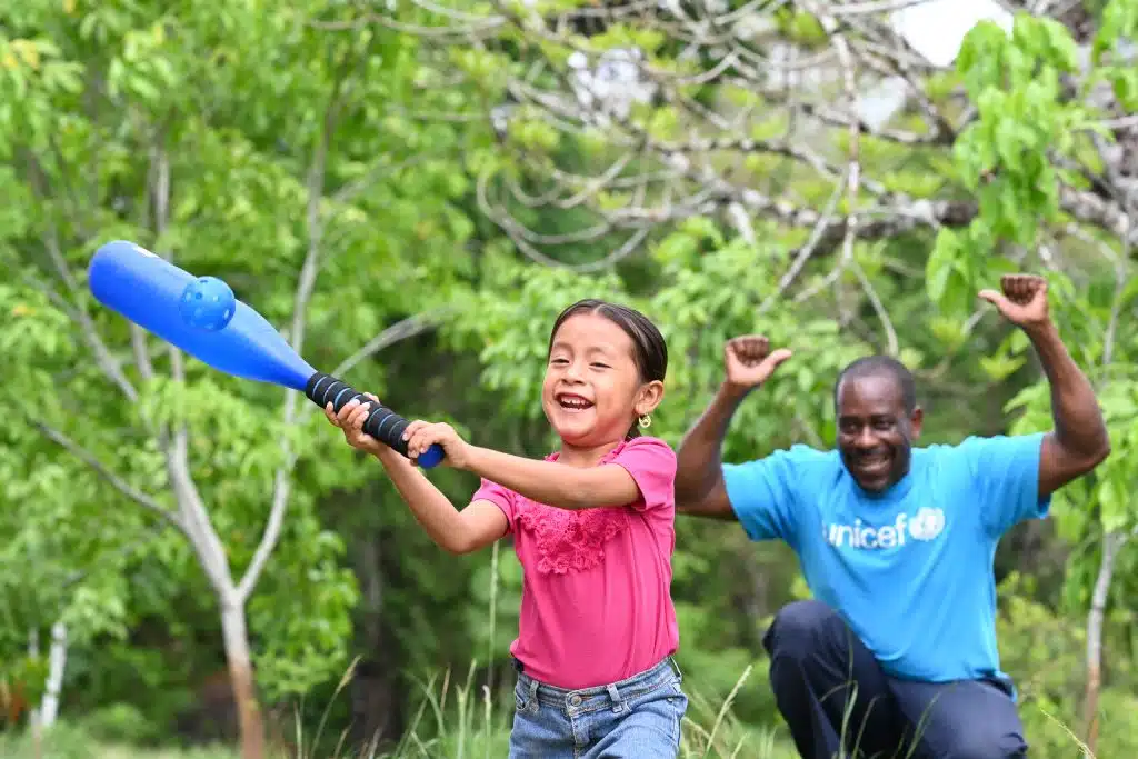 Un membre du personnel de l'UNICEF joue au baseball avec Oneida, 5 ans, dans le village d'Otoxha, au sud du Belize. Sur place, l'UNICEF a mis en place un programme de protection sociale. © UNICEF/UNI594461/Dejongh