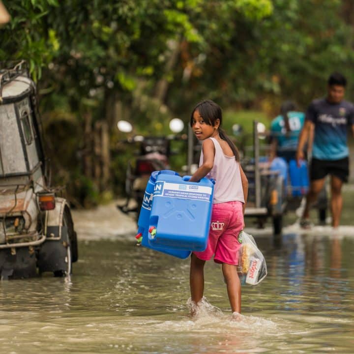 Une petite fille transporte des bidons d'eau potables fournis par l'UNICEF et ses partenaires dans une rue inondée de Camarines Sur, aux Philippines, le 31 octobre 2024. ©UNICEF/UNI680390/San Diego