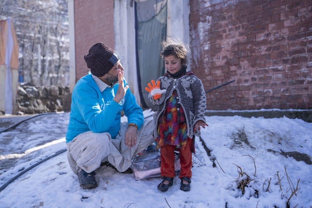 Zaheer Ahmad, responsable de la planification, du suivi et de l'évaluation à l'UNICEF, s'entretient avec Wajiha, 6 ans, lors de la distribution de kits d'hiver aux enfants touchés par les inondations à Sheringal, au Pakistan. © UNICEF/UN0779320/Khan