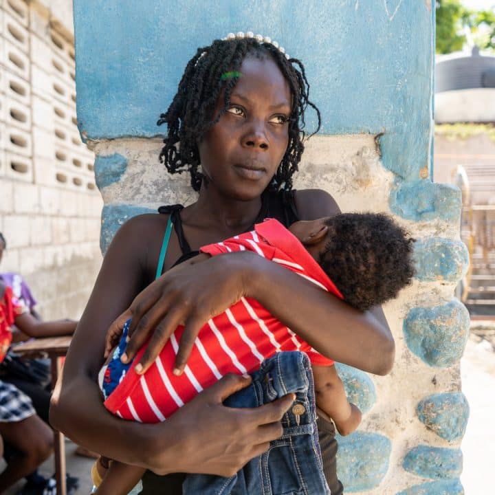 Tamaila Augustin, déplacé par le massacre de Pont Sondé, porte son enfant dans la cour de l'école nationale Antoinette Dessaline. © UNICEF/UNI662616/Erol